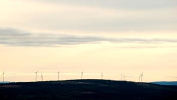 Kvällshimmel över skogslandskap, med vindkraftverk längst i bakgrunden.