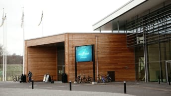 Bild på Skövde Arenas ingång, med träpaneler som blir en kontrast mot huvudbyggnadens glasfasad.