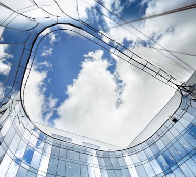 Jarlahuset seen from the ground and up to the air, with its glass walls shaping up a quadrant with rounded walls.
