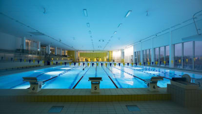 Inside Hylliebadet, Malmö. A lit up swimming pool among darkness both inside and outside.