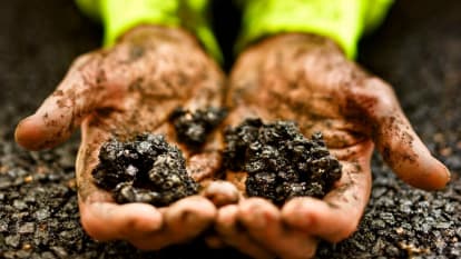 Picture of dirty hands holding pieces of NCC Viaco Asphalt