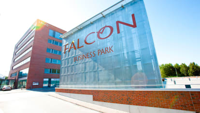 The Falcon Business Park building is in the background to the left, with red cinderblock walls. In the foreground is a large, textile-made sign denoting the business park.