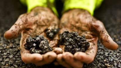 Picture of dirty hands holding pieces of NCC Viaco Asphalt