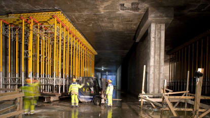 Inuti Malmös Citytunnel, under uppbyggnad. Byggarbetare strövar omkring, och stödfundament för betong samt byggplank syns.