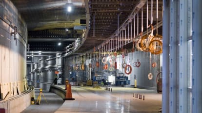 A station inside Malmös Citytunneln under construction. Cords for the station lights are hanging from the roof, and machines are working in the background.