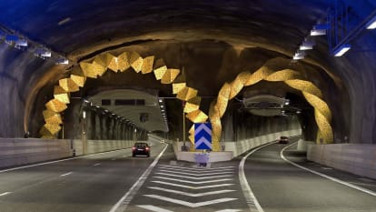 Inuti Södra Länken, Stockholm. Sprutbetongtäckta tunnelväggar lyses upp i blått, med dekoration där avfarten svänger från huvudvägen.