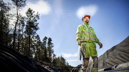 En arbetare står vid en utgrävd vall och blickar bortåt mot kamerans håll. Bland honom finns nyinstallerade likströmskablar.