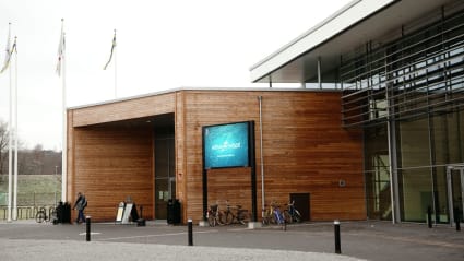 Bild på Skövde Arenas ingång, med träpaneler som blir en kontrast mot huvudbyggnadens glasfasad.