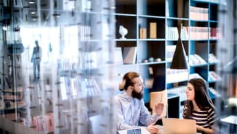NCC har fem affärsområden. På bilden ser du två personer som diskuterar i en biblioteksliknande miljö.
