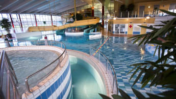 Stor badanläggning med upphöjd bubbelpool närmast kameran, och äventyrsbad med rutschkanor av olika storlek.