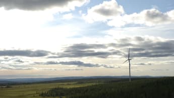 Ett enstaka vindkraftverk virvlar på ett utbrett landskap.