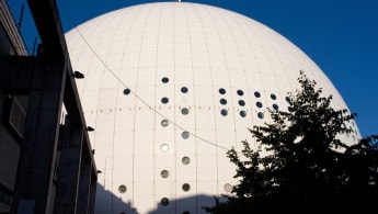 The Stockholm Globe rises from the ground, partially blocked by buildings and trees.