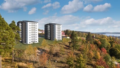 Två flerbostadshus som står vid en slänt mot skog och vatten.