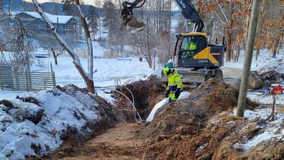 En grävmaskin gräver i marken för utbyggnad av VA-nät, i vinterskrud.