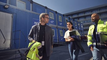 Tre personer studerar en skiss tillsammans. I bakgrunden syns en whiteboard med skrivelser.