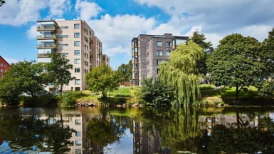 Bostadsrättter i Ängelholm längs en flod med träd i närheten.