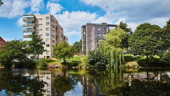 Bostadsrättter i Ängelholm längs en flod med träd i närheten.