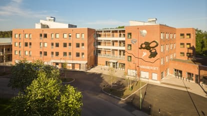 Bild på uppbyggnad av flera hus, en bilväg och blå himmel.