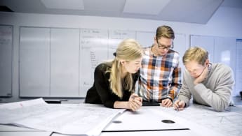 Three partners are looking at a technical drawing, with a used whietboard in the background.