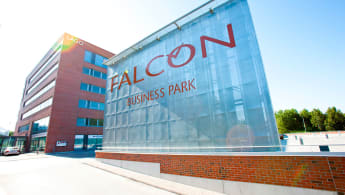 The Falcon Business Park building is in the background to the left, with red cinderblock walls. In the foreground is a large, textile-made sign denoting the business park.
