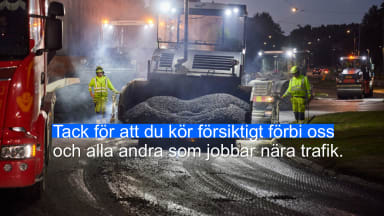 Bilden visar en asfaltlläggare framifrån, på varje sida om läggaren går en person i varselkläder och styr läggaren. Det är mörkt ute och alla lampor och ljus syns tydligt. Texten i bilden lyder: Tack för att du kör försiktigt förbi oss och alla andra som jobbar nära trafik.