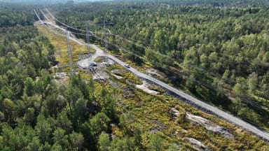 Bilden är ett flygfoto d'r man ser en kraftledning över en ledningsgata i skogen.