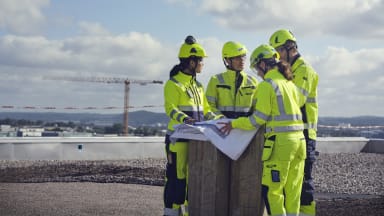 Flera NCC-medarbetare står på ett tak och tittar på en ritning.