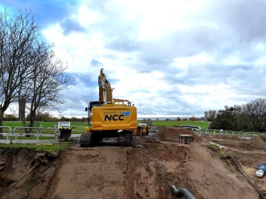 Grävmaskin på arbetsplats, träd och natur i bakgrunden.