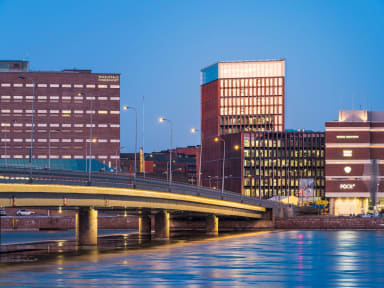 Nighttime view of We Land, other buildings and bridges, seen across a body of water.