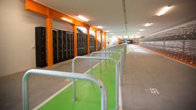 På bilden syns ett långt cykelgarage med många angöringsplatser och förvaringsskåp till vänster.