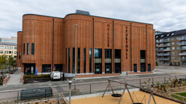 Illustration av en idrottshall omvigen av träd och gångväg.