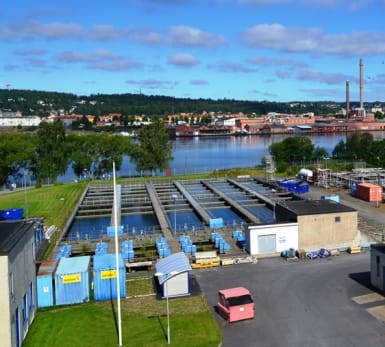 Simsholmens avloppsreningsverk. Stora utomhusbassänger och små fordonsgarage, med Jönköping över sjön i bakgrunden.