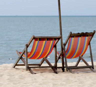 Bild på två tomma solstolar på en strand, med havet i bakgrunden.