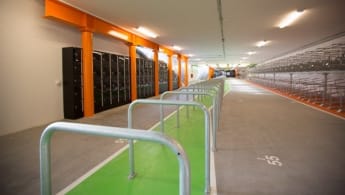 På bilden syns ett långt cykelgarage med många angöringsplatser och förvaringsskåp till vänster.