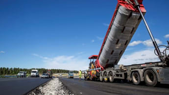 Machineries and workers pave the new E18 road, with the forest visible in the background.