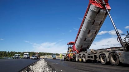 Machineries and workers pave the new E18 road, with the forest visible in the background.