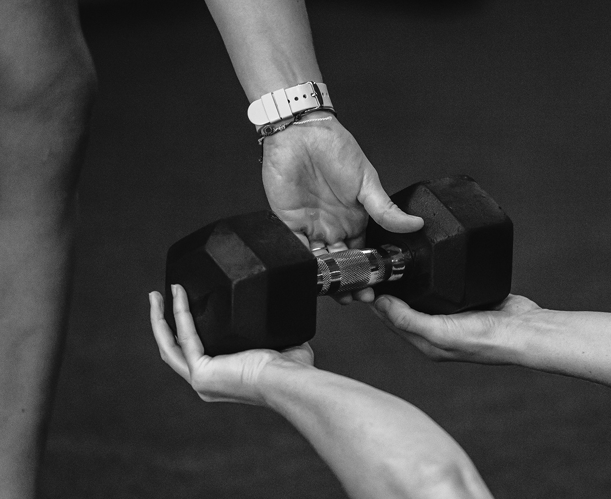 A trainer hands a dumbbell to a person working out.