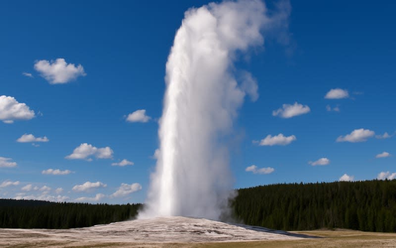 A breathtaking view of the Old Faithful geyser erupting under a clear blue sky with scattered clouds.