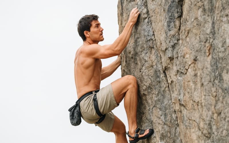A climber attempting to climb a rock face without a helmet, visibly missing essential gear.