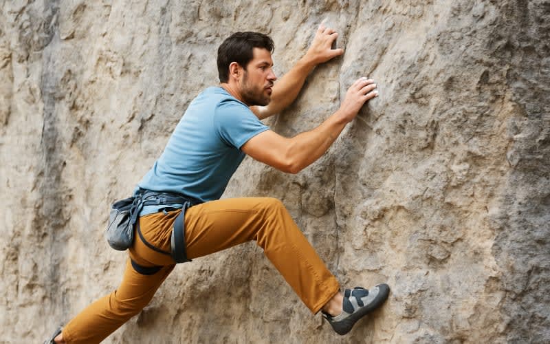 A climber using incorrect hand placements and foot positions on a rock face