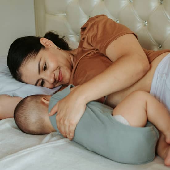 A joyful mother cuddles her newborn in a soft, sunlit bedroom—highlighting the beauty of post-pregnancy life. This image reflects the emotional and physical journey of motherhood. In this AEDITION article we cover non-invasive mommy makeover treatments aimed at helping women restore confidence and feel their best after childbirth.
