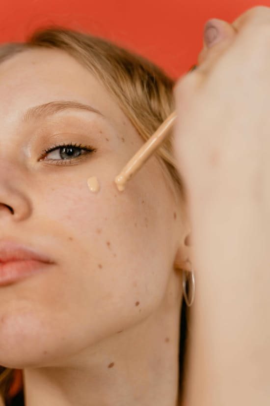 A close-up photo of a young woman applying tinted spf moisturizer to her face, focusing on her cheek. Her skin looks fresh and dewy, with a natural glow.  The texture of the tinted moisturizer is sheer and lightweight. 