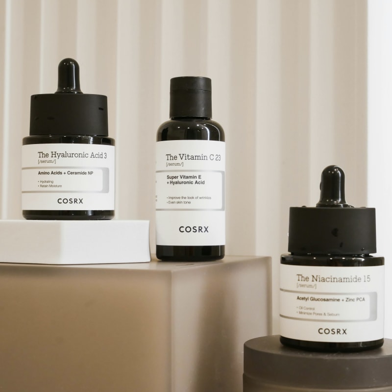 COSRX K-beauty serums displayed on neutral-toned platforms, featuring The Hyaluronic Acid 3, The Vitamin C 23, and The Niacinamide 15. These popular Korean skincare products highlight essential ingredients like hyaluronic acid, vitamin C, and niacinamide, representing the latest trends in K-beauty for hydration, brightening, and pore care. AEDITION article Korean Skincare Explained: Everything You Need to Know About K-Beauty Trends, Products, and Routines