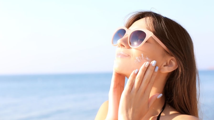 Woman in sunglasses putting on sunscreen by the sea.