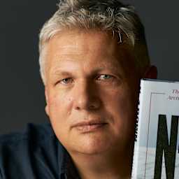 The image shows a middle-aged man with gray hair holding up a book titled "N-4 Down" against a dark background.
