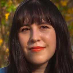 A young woman with dark hair and a warm smile stands in a vibrant autumn landscape, surrounded by yellow flowers and lush greenery.