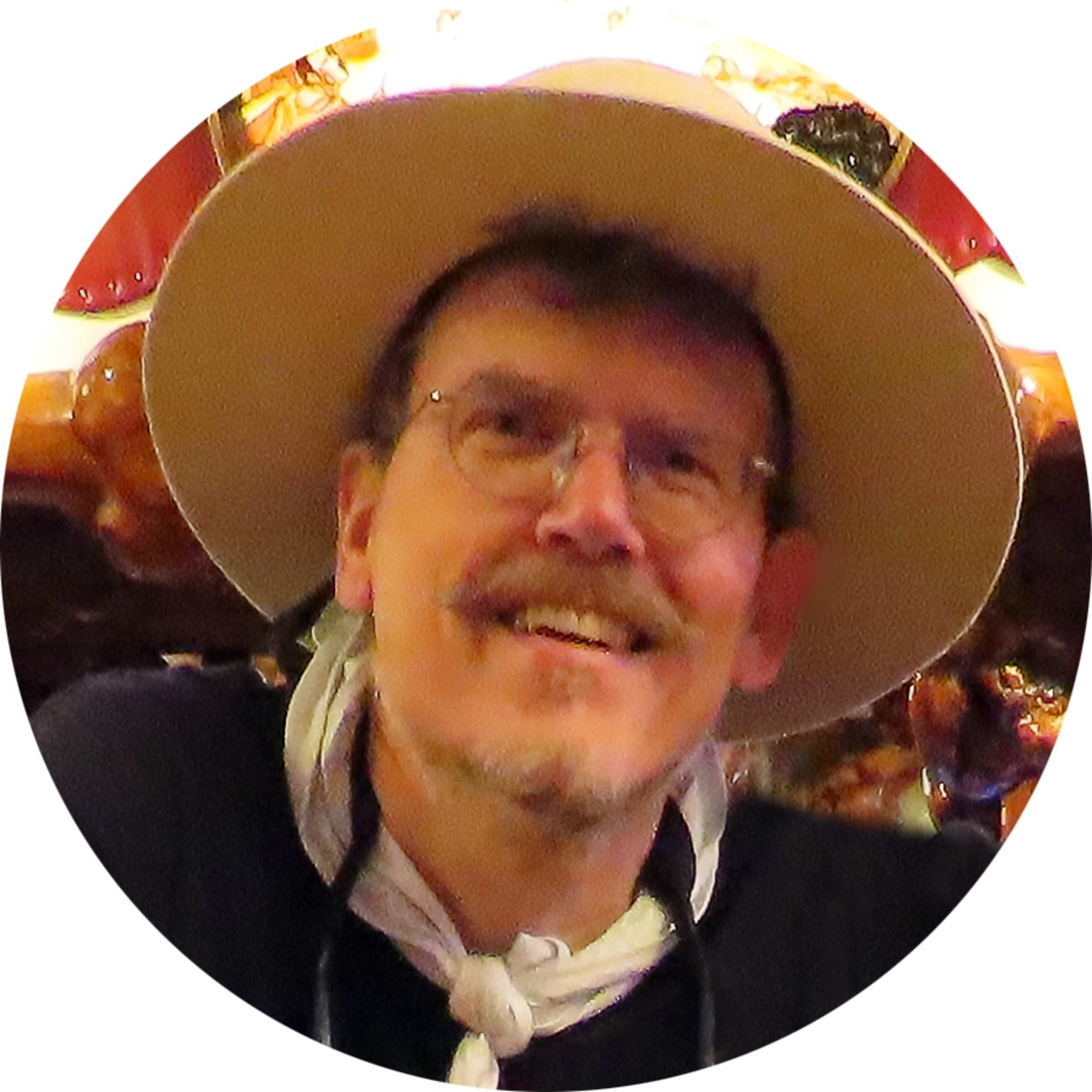 A smiling man wearing a cowboy hat and a white shirt stands in front of a colorful background.