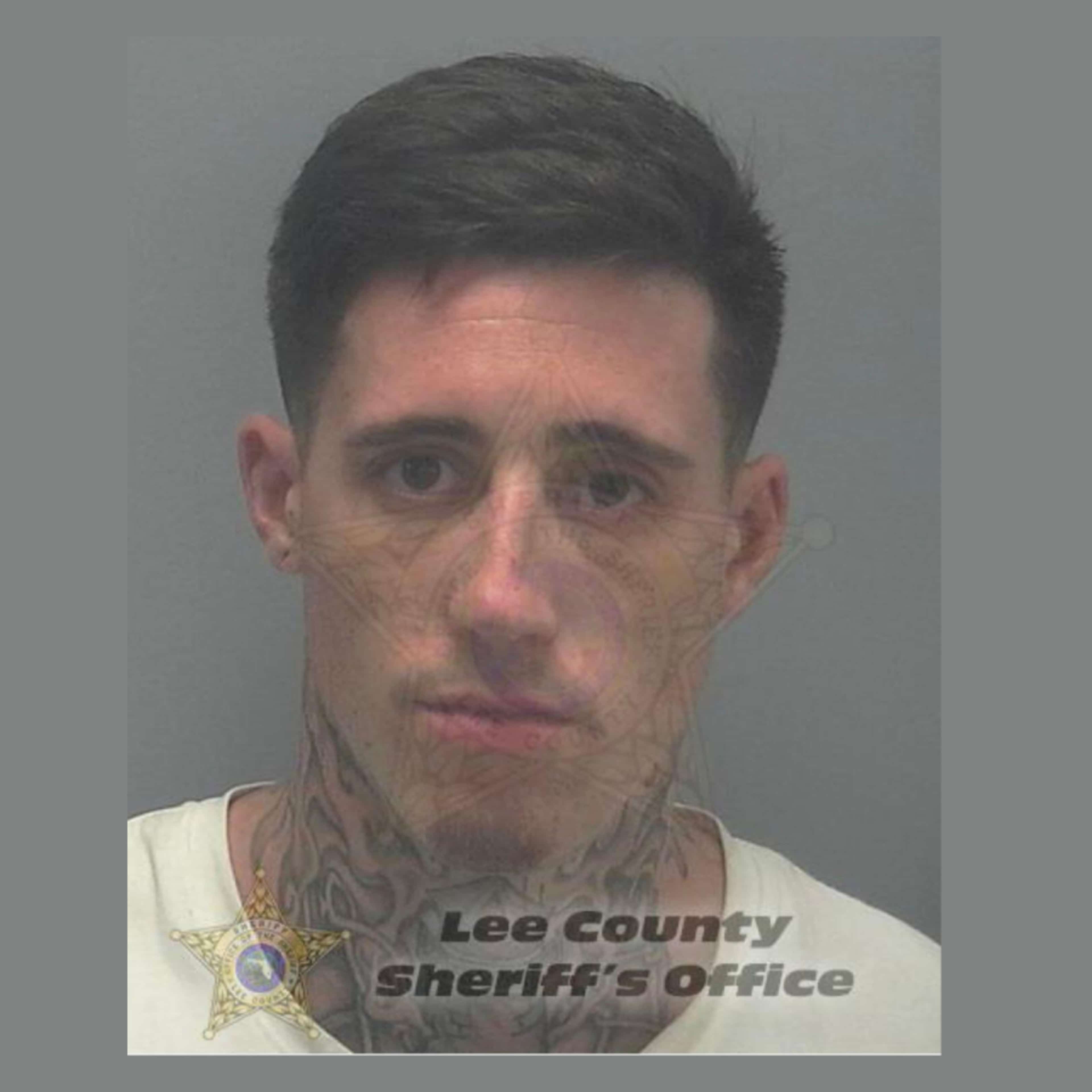 The image shows a close-up portrait of a man with a serious expression, wearing a white shirt and a badge indicating he is from the Lee County Sheriff's Office.