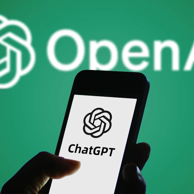 In this photo illustration, the logo of ChatGPT is displayed on a smartphone screen with an OpenAI logo in the background on a green screen