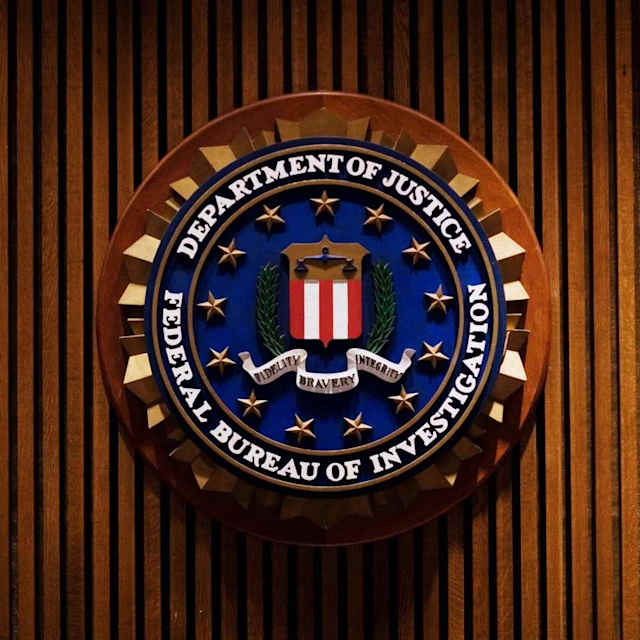 A wooden plaque with the seal of the United States Federal Bureau of Investigation (FBI) is displayed against a backdrop of wooden paneling.